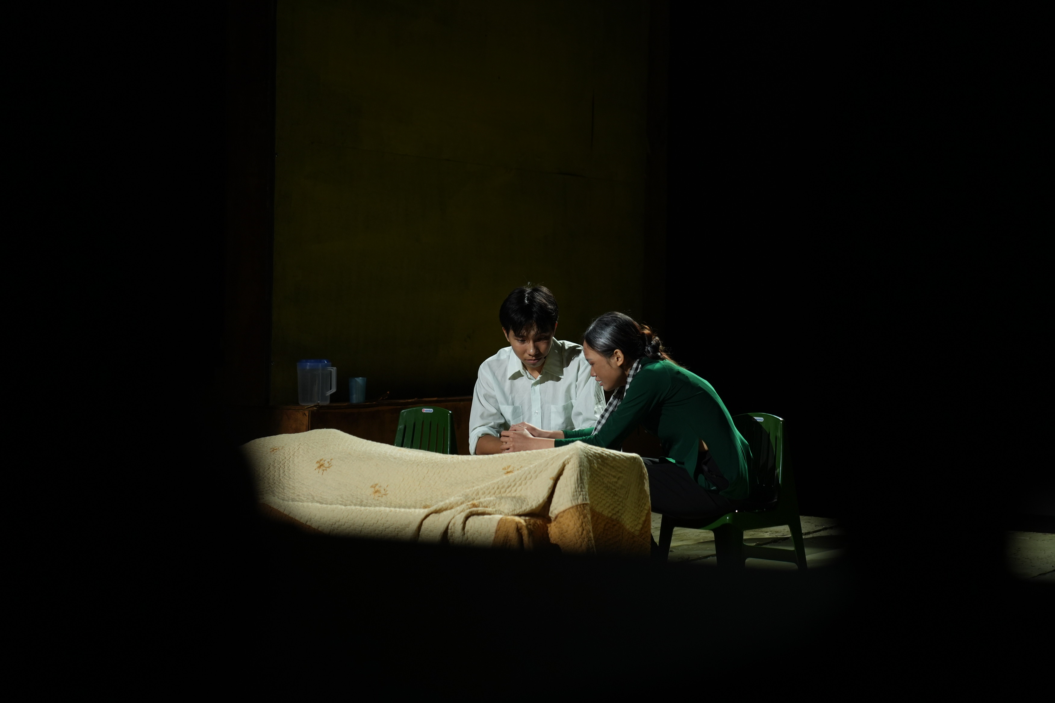 A quiet bedside scene lit against a dark stage