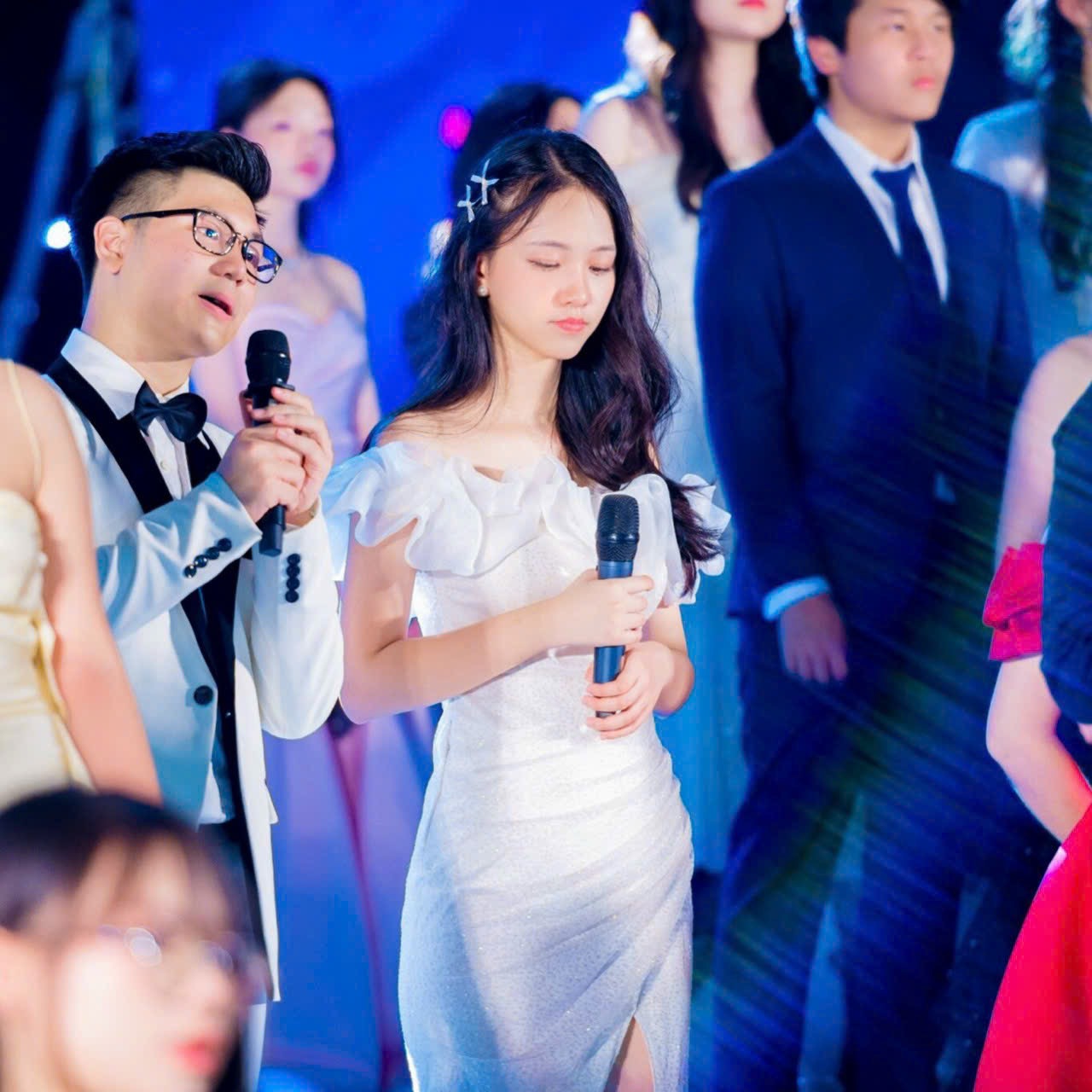 Gia Han in a white dress singing a duet at a Glee Ams show