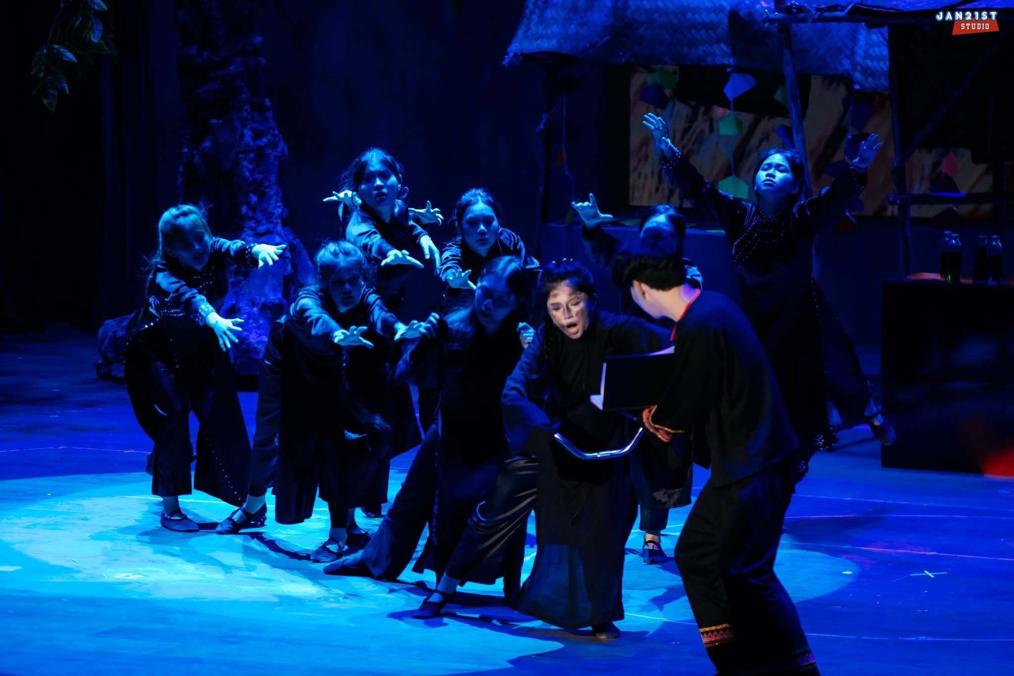The cast mid-scene under deep blue stage light